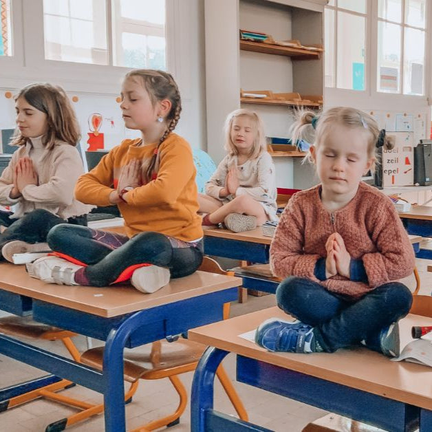 leerlingen die yoga doen en mediteren op hun tafel in de klas