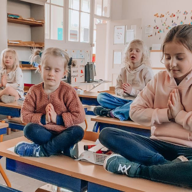 kinderen die op hun tafel in de klas yoga doen